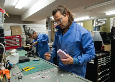 Two engineers in blue lab coats working at a bench with hand tools