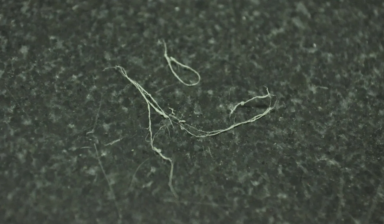 Macro photograph of fine fibres shed from the molded bottle lip, shown against a dark background