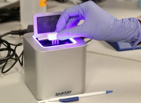 Gloved hand loading a sample cartridge into the Spartan Cube DNA analyzer lit purple