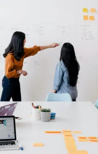 Two people reviewing sketches on a whiteboard above a desk with sticky notes