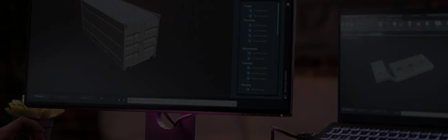 Dimmed workstation monitors showing CAD models of a shipping container and a flat part
