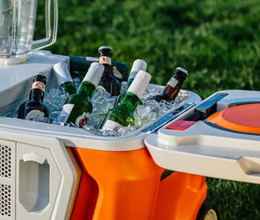 Orange rolling cooler full of ice and bottled drinks with a built-in blender on a lawn