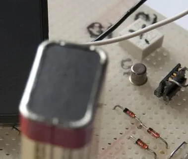Close-up of a 9-volt battery and components on a prototype perfboard circuit