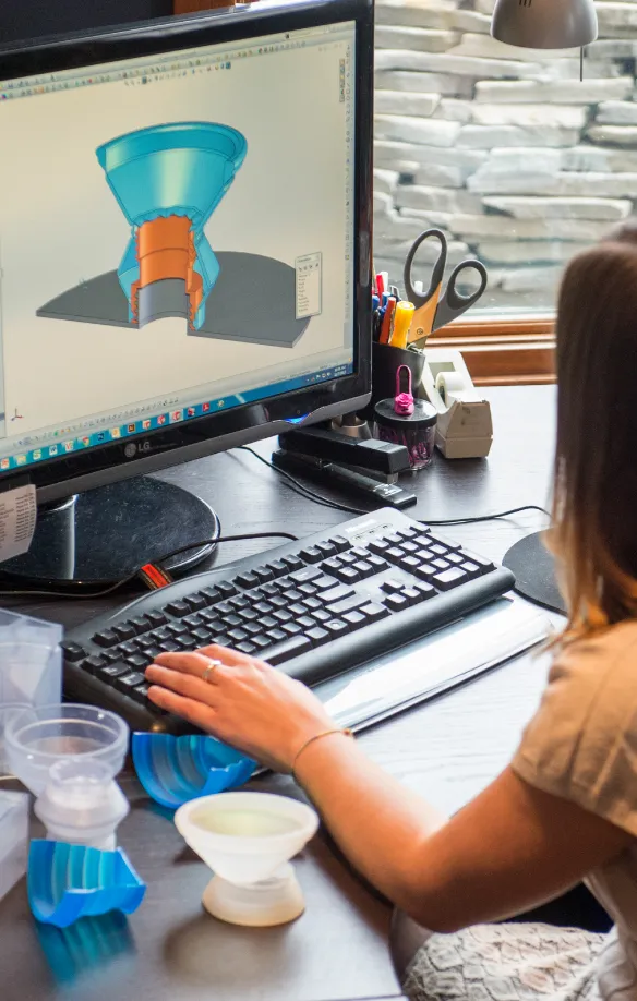 Designer at a workstation with a CAD model of a funnel part and 3D-printed prototypes