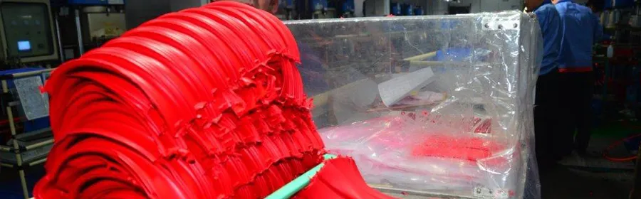 Stack of red moulded plastic parts beside a machine on a factory floor