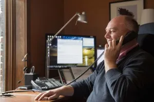 Man on the phone at a home office desk with a computer monitor