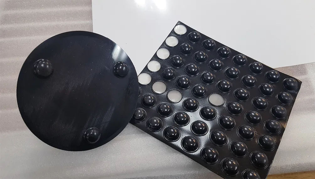 3D printed black coffee filter holder with rubber feet beside a sheet of adhesive bumpers