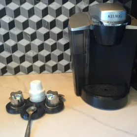 3D-printed coffee filter holder holding reusable K-cup pods beside a Keurig coffee maker