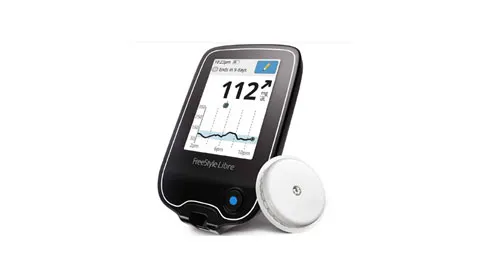 Abbott FreeStyle Libre glucose reader showing a reading of 112 beside its round sensor