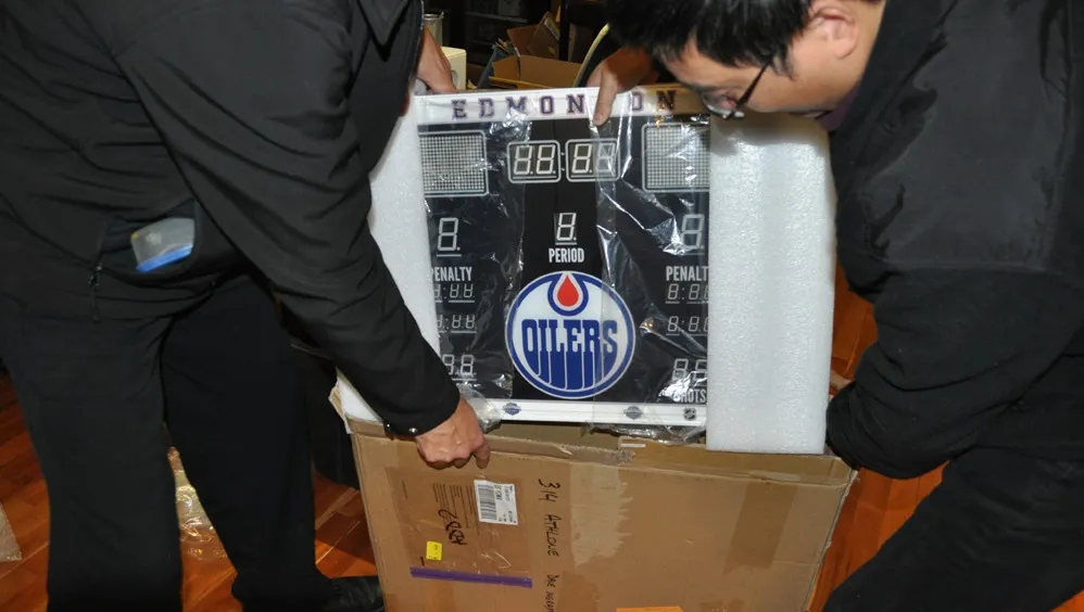 Two people unboxing a production Edmonton Oilers Fantasy Scoreboards unit from its shipping box