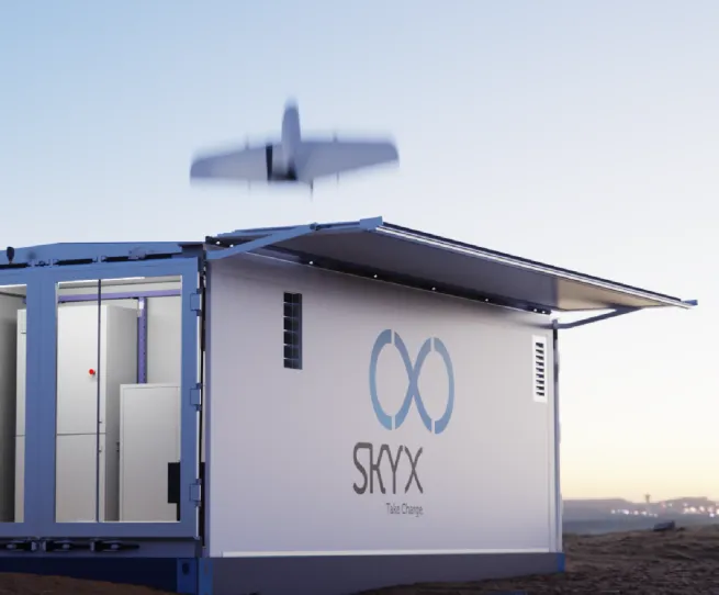 SkyX drone flying over its container-sized docking station at dusk