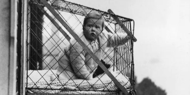 Vintage photo of a baby sitting in a wire cage hung outside an apartment window
