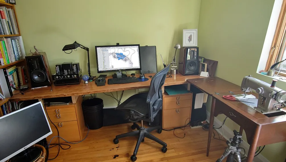 Home office desk with a monitor showing a CAD model, speakers and a sewing machine