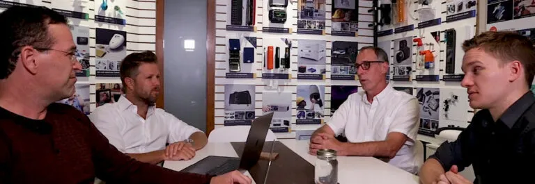 Four people in discussion around a table in the Design 1st office, product samples on the wall behind