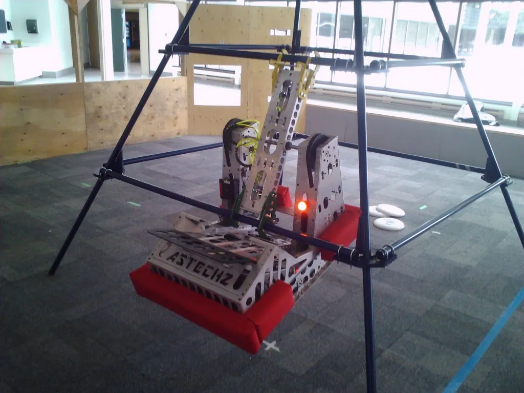 Astechz Team 2994 robot hanging from a pyramid frame during a climbing test