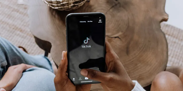 Illustration of hands holding phones around a TikTok video with shirt, cap, mug and coin icons