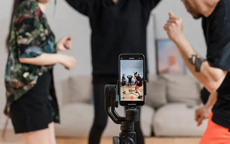 Three people dancing in a living room while a phone on a gimbal records them