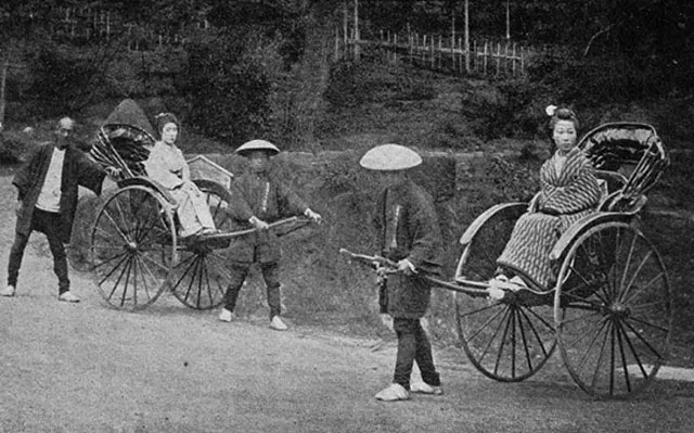 Black-and-white photograph of two Japanese rickshaws, each pulled by a man, carrying seated passengers