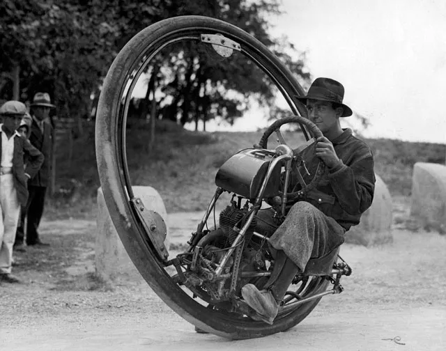 Black-and-white photo of a man riding a gas-powered monowheel, seated inside its single large wheel