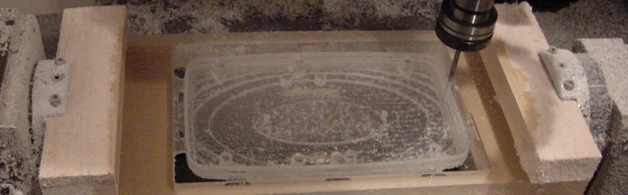 CNC mill cutting a clear plastic enclosure prototype held in a wooden fixture