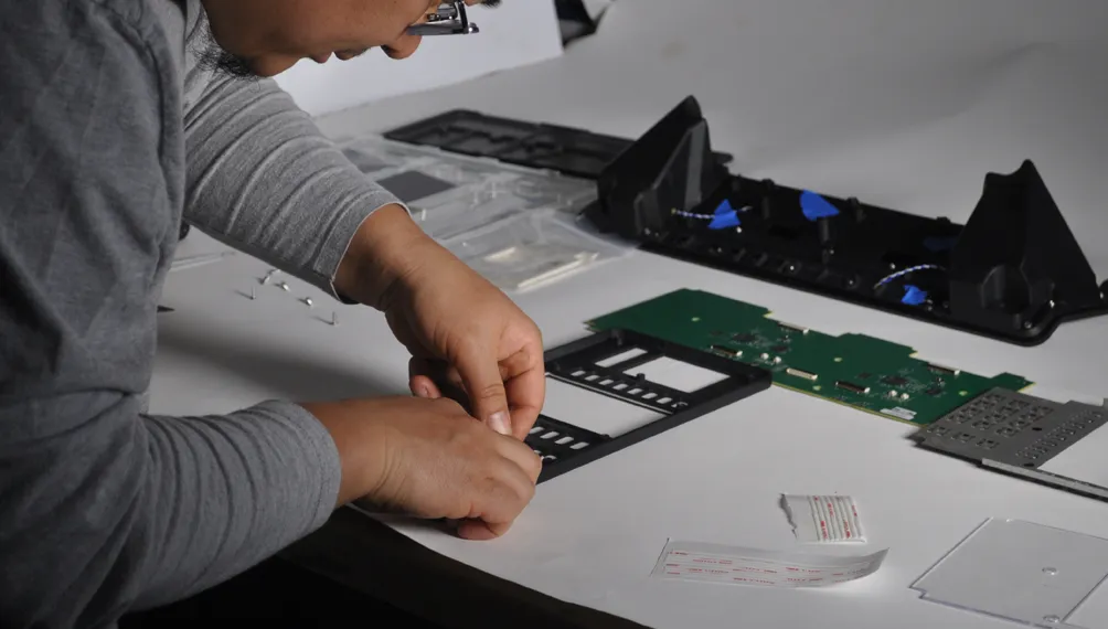 Engineer assembling a Cloud9 keypad frame beside a circuit board and housing parts