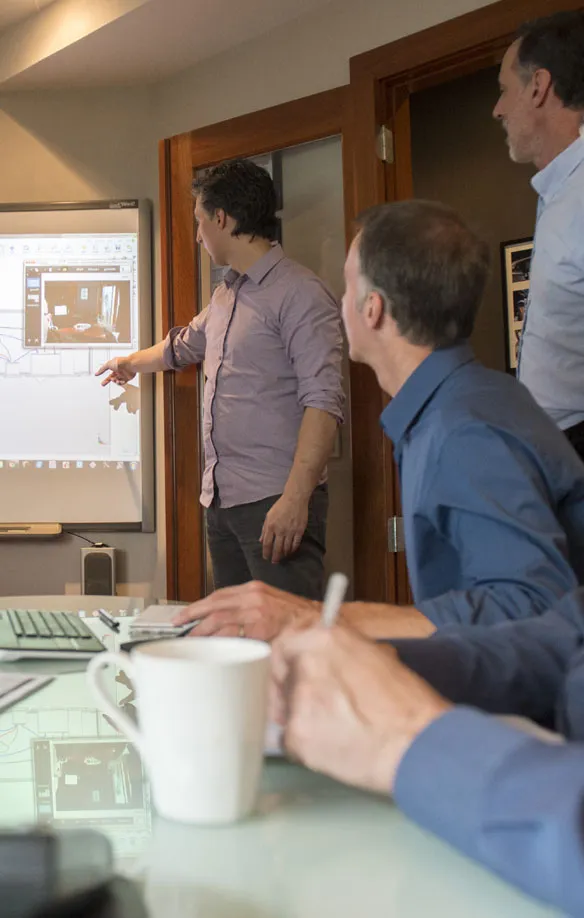 Designer pointing at a design on a whiteboard screen while two colleagues watch