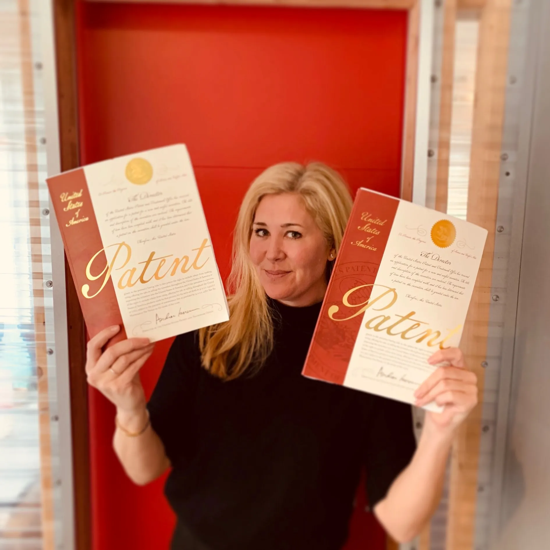 Woman holding up two United States patent certificates in front of a red door