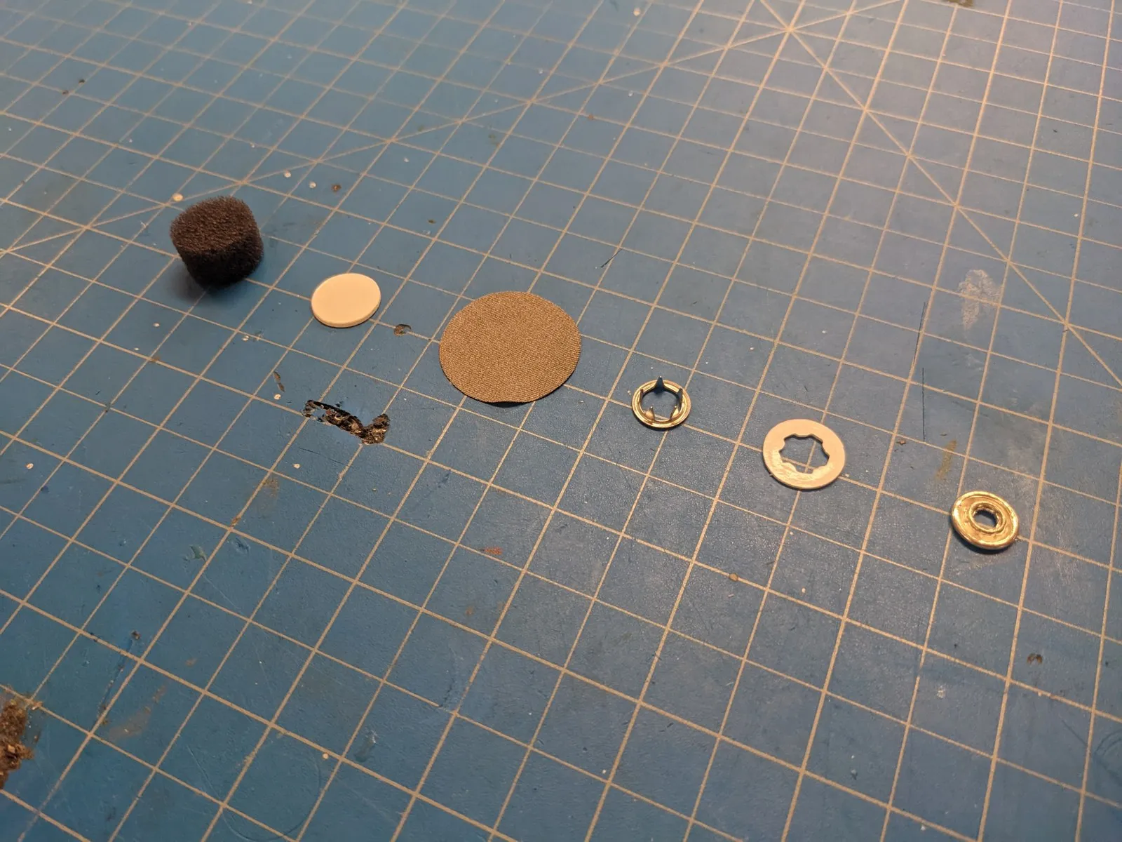 Neurovine electrode parts on a cutting mat: foam, discs, snap ring and rivet